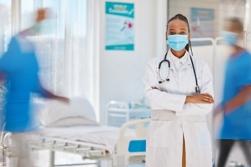 Image showing Portrait, covid and healthcare with a doctor black woman arms crossed in a busy hospital for service. Trust, medical and mask with a female medicine professional working in a clinic for health