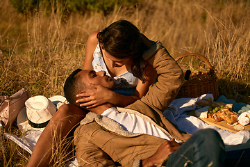 Image showing Love, sunset and picnic with couple in field for summer break, relax and romantic date. Happy, kiss and food with man and woman affectionate in grass of countryside for travel, bonding and peace