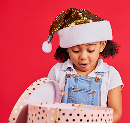 Image showing Christmas, gift and girl child surprise, wow and curious in studio, happy and shock against red background. Box, present and excited toddler express omg, cheer and happiness for festive celebration