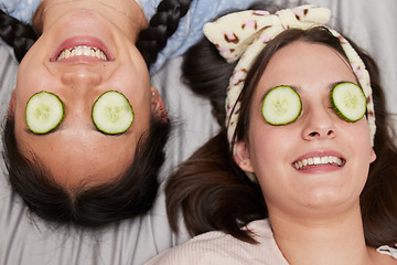 Image showing Friends, facial and skincare with cucumber by women relax, spa day and bonding while lying on a bed together. Beauty, girl and skin treatment with fruit, product and organic face mask in their home