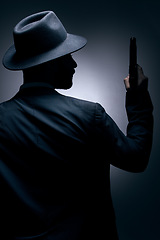 Image showing Gangster, silhouette or holding gun on studio background in secret spy, isolated mafia leadership or crime security. Model, man or dark hitman and weapon suit, fashion clothes or bodyguard aesthetic