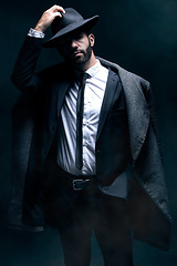 Image showing Fashion, portrait and a man in a dark studio with confidence, clothes and a hat for vintage style. Model person in a suit and coat for winter, business or mystery as a spy on a black background