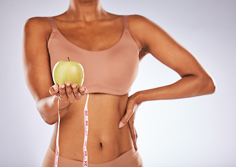 Image showing Apple, measuring tape and diet with a black woman in studio on a gray background for weightloss. Food, fitness and health with a female posing to promote exercise, nutrition or health eating