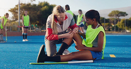 Image showing Woman, sports and knee injury in hockey training, practice or game on a blue turf with coach and team. Sport mentor helping female in leg pain, accident or bruise from physical activity during match