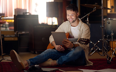 Image showing Digital tablet, guitar and man in a recording studio for music production or acoustic performance. Musician, artist and happy male guitarist on a mobile device with a musical string instrument.