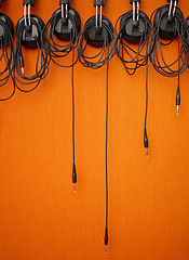 Image showing Audio, cables and mockup on an orange wall background in a music studio for recording or sound engineering. Media, equipment and hanging wires in an empty room of a record label for production