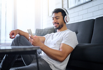 Image showing Phone, music and man with headphones in home living room streaming radio or podcast. Cellphone, technology and male in lounge sitting on floor listening to song, audio or album on mobile smartphone.