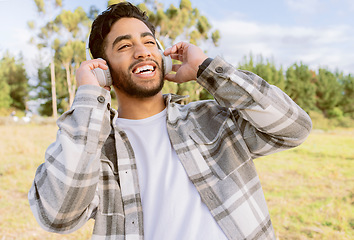 Image showing Happy, man and music with headphones in forest, laugh and relax on blue sky, tree and space background. Radio, earphones and guy, smile and joy while listening to audio, podcast or track in nature