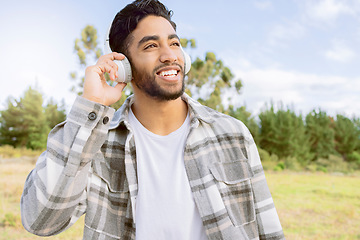 Image showing Music, smile and man with headphones in forest, happy and relax on blue sky, tree and space background. Radio, earphones and guy, smile and joy while listening to audio, podcast or track in forest