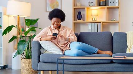 Image showing Laughing woman listening to music and sending a message with funny memes on her phone and drinking coffee while on the sofa. Happy black female browsing social media and surfing the internet online