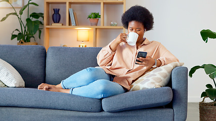 Image showing Laughing woman listening to music and sending a message with funny memes on her phone and drinking coffee while on the sofa. Happy black female browsing social media and surfing the internet online