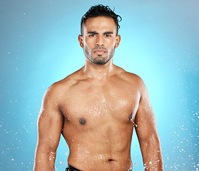 Image showing Water splash, portrait and man in studio for skincare, wellness and grooming on blue background. Cleaning, beauty and moisture by Mexican model relax with luxury, routine and body care while isolated