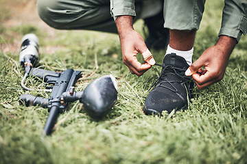 Image showing Paintball, gun and shooter or man kneeling ready for competitive match or competition in the forest. Player, athlete and person tying laces with game equipment or weapon on a sports field
