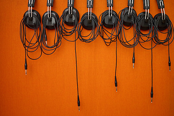 Image showing Audio, music and headphones hanging on a wall for a dj, podcast or radio production in the studio. Sound, electronics and equipment for streaming songs, listening to a track or musical accessory