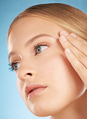 Image showing Face of beautiful woman, cosmetic skincare on blue background in studio and side profile with hand on temple. Young blonde model with clean finger nails, luxury beauty product and natural makeup