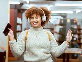 Image showing Music, dance and headphones with a student black woman listening to the radio in a university library. Phone, internet and a young female college pupil streaming audio while dancing or having fun