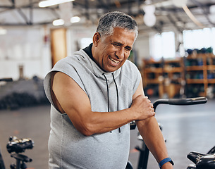 Image showing Sports, gym and injury, old man with arm pain, emergency during workout at fitness studio. Health, wellness and inflammation, senior person with hand on muscle cramps while training on exercise bike.