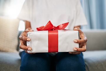 Image showing Box, gift and woman on a sofa in the living room with a giving gesture for celebration or event. Bow, wrapping paper and African female with a present for christmas, birthday or holidays in a house.