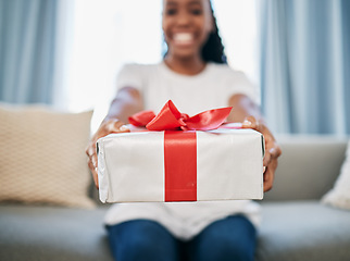 Image showing Christmas, gift and a box in the hands of a black woman in her home, sitting on the living room sofa. Birthday, present and event with a female giving a package during a celebration surprise