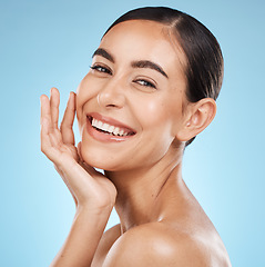 Image showing Portrait, hand and smile with a model woman in studio on a blue background for beauty or skincare. Face, skin and cosmetics with an attractive young female posing to promote a luxury product