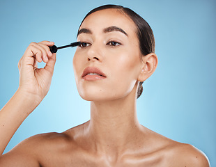 Image showing Mascara, application and woman with makeup on face isolated on a blue background in a studio. Beauty, glam and model with cosmetics from a brush on an eyelash for facial treatment on a backdrop