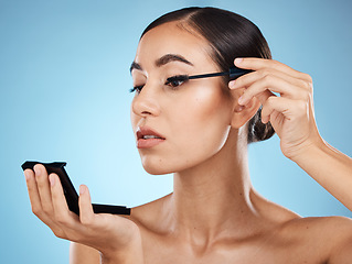 Image showing Mascara, application and woman with makeup and mirror isolated on a blue background in a studio. Skincare, beauty and model with cosmetics for an event, party or fancy celebration on a backdrop