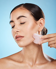 Image showing Face massage, gua sha and skin care woman for dermatology, cosmetics and wellness. Young aesthetic model person for natural stone spa product for facial glow, lines and to relax on blue background