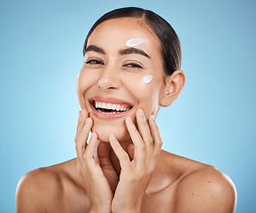 Image showing Portrait, hands and cream with a woman in studio to apply treatment on a blue background for beauty. Face, skincare and lotion with an attractive young female posing to promote a luxury product