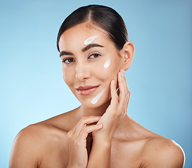 Image showing Portrait, beauty and cream with a woman in studio to apply treatment on a blue background for skincare. Face, skin and lotion with an attractive young female posing to promote a luxury product