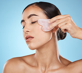 Image showing Skin care, facial massage and beauty woman with gua sha for dermatology, cosmetics and wellness. Young model person with natural stone or spa face product to relax and glow on blue background