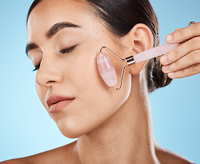 Image showing Skin care, face roller and beauty woman with facial massage for dermatology, cosmetic and wellness. Young aesthetic model person for natural rose quartz spa product to relax on blue background