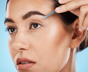 Image showing Hair removal, tweezer and woman doing her eyebrows in studio for beauty, facial and grooming routine. Cosmetics, depilation and female model plucking face hair with cosmetic tool by blue background.