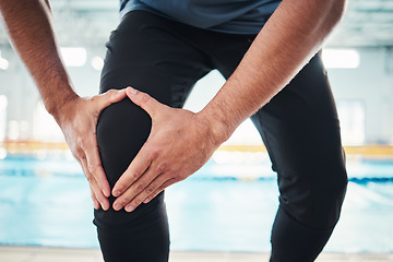 Image showing Hands, knee injury and swim instructor holding his joint in pain with a swimming pool in the background of a gym. Fitness, coach or anatomy with a sports man suffering from a sore leg during exercise