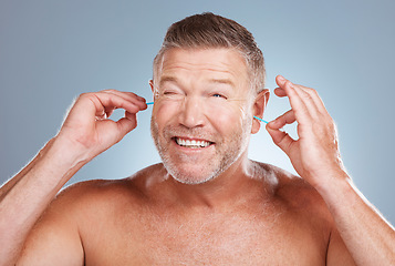 Image showing Earbuds, grooming and man cleaning his ears in a studio for self care, hygiene and cleanliness. Health, wellness and mature guy doing his morning body care routine isolated by a gray background.