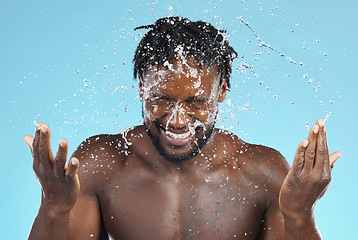 Image showing Water splash, cleaning and hygiene with a model black man in studio on a blue background for hydration. Bathroom, skincare and wellness with a young male wahsing his face for natural skin treatment