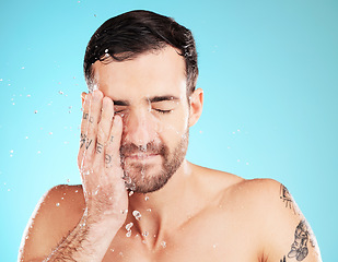 Image showing Water drop, skincare and man with hand on face, morning cleaning treatment isolated on blue background. Facial hygiene, splash and male model grooming for health, wellness and spa skin care in studio