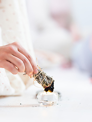 Image showing Woman lighting a smudge kit with herbal stick. Natural elements for cleansing environment from negative energy, adding positive vibes. Spriritual wellness practices.