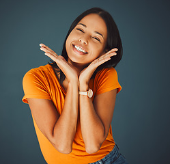 Image showing Woman, happy and hands on face portrait in studio for smile, beauty and motivation for happiness. Model person with orange t-shirt for fashion, positive mindset and mental health on a blue background