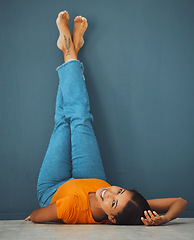 Image showing Woman on floor, smile on face with legs up on wall background and creative pose in studio. Teal copy space, young model laying on ground, portrait of happy person alone and body relaxing aesthetic