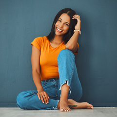 Image showing Black woman, floor and home with smile by wall for clothes, relax and fashion with barefoot. Gen z girl, model portrait and happy in house with feet, jeans and happiness on face by blue background