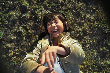 Image showing Headphones, nature and Asian child on the grass to relax, chill and listen to music with freedom. Happy, smile and excited girl kid streaming a podcast or the radio in outdoor field, park or garden.