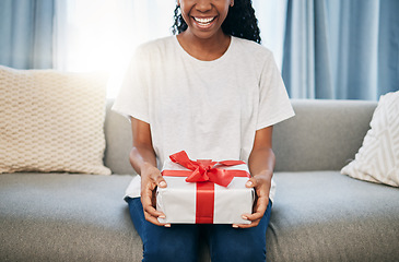 Image showing Present, box and woman on a sofa in the living room with a giving gesture for celebration or event. Bow, wrapping paper and African female with a present for christmas, birthday or holidays in house.