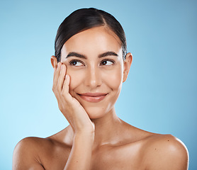 Image showing Woman is thinking, face and happy with beauty, natural cosmetics and glow isolated against blue background. Clean, cosmetic care and hand with facial, makeup and healthy skin with skincare in studio