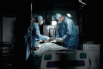 Image showing Surgery, doctors and surgeon in medical theatre for teamwork, expert services or emergency in dark room. Doctors saving patient life on table in hospital theater for healthcare, insurance and support