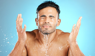 Image showing Water splash, face and man in studio for skincare, wellness and grooming on blue background. Cleaning, beauty and facial by Mexican model relax with luxury, routine and moisture while isolated