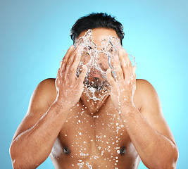 Image showing Man, face and water splash in studio with skincare, wellness and grooming on blue background. Cleaning, beauty and moisture by Mexican model relax with luxury, routine and facial while isolated