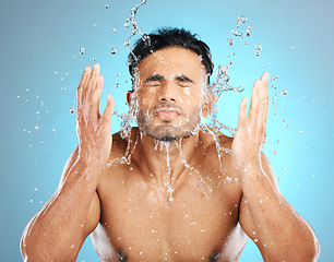 Image showing Facial, water splash and man in studio for skincare, wellness or grooming on blue background. Cleaning, beauty and moisture by Mexican model relax for luxury, routine or face treatment while isolated