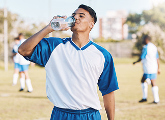 Image showing Drinking water, break and soccer player on a sports field resting after match or competition on a sunny day. Man, athlete and sportsman refreshing during a game happy and smiling for due to fitness