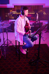 Image showing Artist, headphones or guitar in neon studio, recording production or performance on radio mic, label or band concert. Guitarist, musician or man playing on strings instrument in night light practice