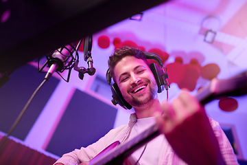 Image showing Happy man, musician or guitar in neon studio, recording production or performance for radio, label or low angle concert. Guitarist, artist or singer playing strings instrument on headphones practice